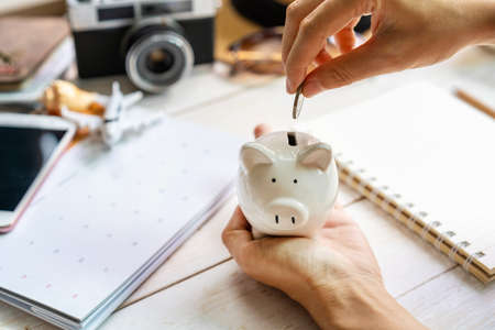 Young traveler holding piggy bank and collecting money and planning a vacation trip and looking for holidays on the calendar, Travel conceptの写真素材