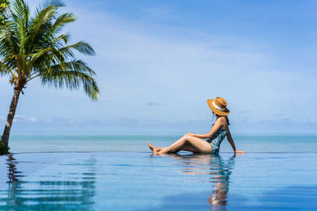 Young woman traveler relaxing and enjoying by a tropical resort pool while traveling for summer vacation, Travel conceptの写真素材