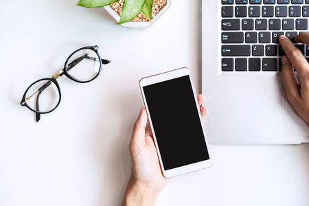 Hand holding empty screen Smart phone on business desk office with copy space, Top view