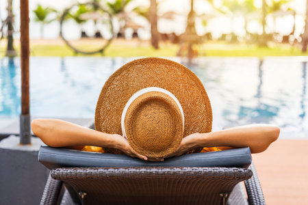 Young woman traveler relaxing and enjoying the sunset by a tropical resort pool while traveling for summer vacationの写真素材