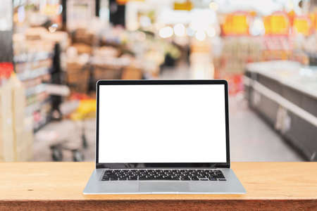 Empty screen laptop on a wooden table with abstract blurred image of supermarket store at the mallの写真素材