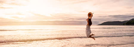Young woman traveler jumping and enjoying beautiful Sunset on the tranquil beach, Travel on summer vacation concept, Banner panoramaの写真素材