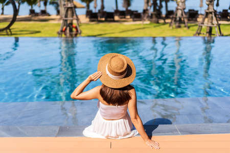 Young woman traveler relaxing and enjoying by a tropical resort pool while traveling for summer vacationの写真素材