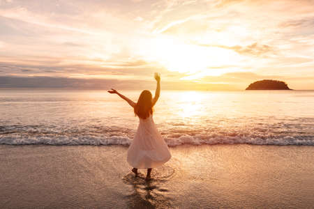 Young woman traveler dancing and enjoying beautiful Sunset on the tranquil beach, Travel on summer vacation conceptの写真素材