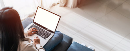 Young woman using laptop and relaxing on sofa in living room at cozy home in the morningの写真素材