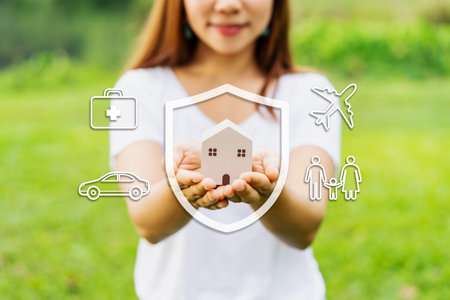 Young woman holding wooden house model with car, family, travel and health insurance icons and conceptの写真素材