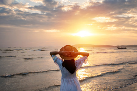 Young woman traveler relaxing and enjoying the beautiful sunset on the tranquil beach, Travel on the summer vacation conceptの写真素材