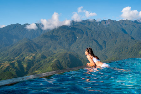 Young woman traveler relaxing in sky pool and looking at the beautiful nature landscape with blue sky and mountains in Sapa, Vietnamの写真素材