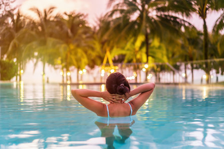 Young woman traveler relaxing and enjoying the sunset by a tropical resort beachfront pool while traveling for summer vacationの写真素材