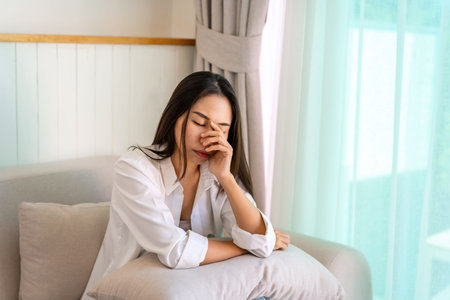 Lonely young Asian woman feeling depressed and stressed in living room at home, Negative emotion and mental health conceptの写真素材