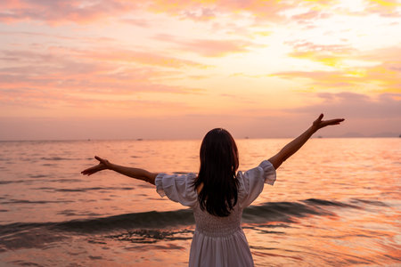 Young Asian woman traveler relaxing and watching beautiful Sunset on the tranquil beach, Travel on summer vacation conceptの写真素材