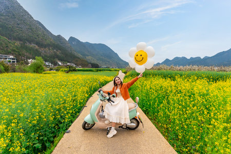 Young happy woman tourist enjoying the canola fields and mountains while traveling in Wanfenglin, Chinaの写真素材