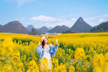 Young happy woman tourist taking selfie and enjoying the canola fields while traveling in Luoping, Chinaの写真素材