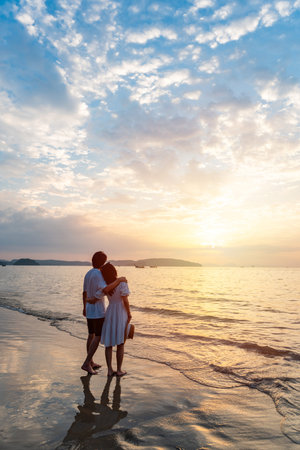 Young happiness Asian couple traveler relaxing and watching beautiful Sunset on the tranquil beach, Traveling on summer vacation conceptの写真素材