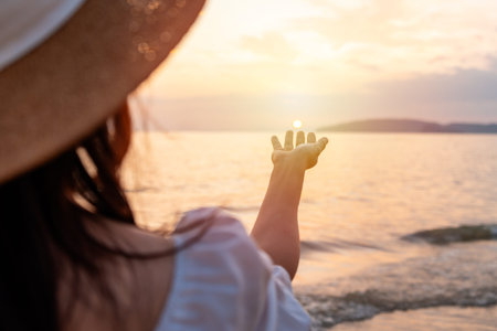 Young woman's hand reaching for the Sun during beautiful sunset at the tranquil beachの写真素材