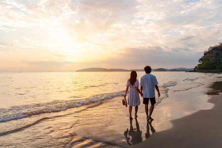Young happiness Asian couple traveler relaxing and watching beautiful Sunset on the tranquil beach, Traveling on summer vacation conceptの写真素材
