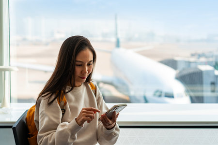 Young Asian woman traveler using smart phone while waiting for her flight at the airportの写真素材
