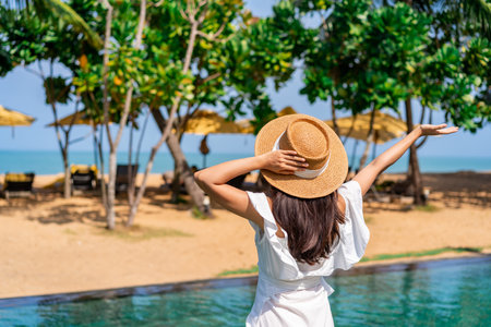 Young woman traveler relaxing and enjoying the beach view by a tropical resort pool while traveling for summer vacation, Travel lifestyle conceptの写真素材