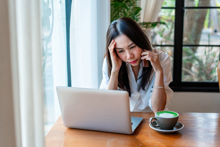 Stress young Asian business woman working with laptop in cafeの写真素材