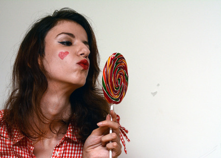 A happy, female model enjoying a lollipop and a heart on her cheek.の写真素材