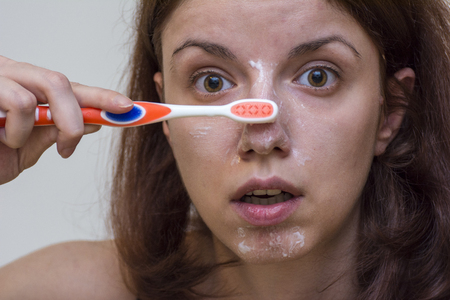 Redhead model using toothbrush and toothpaste to clean the black heads on her faceの写真素材