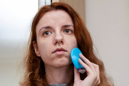 red head woman using a facial cleansing brush for a morning routine and muscle toningの写真素材