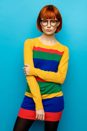 Fashion photo of young woman with red hair wear colorful dress and glasses, isolated on blue backgroundの写真素材