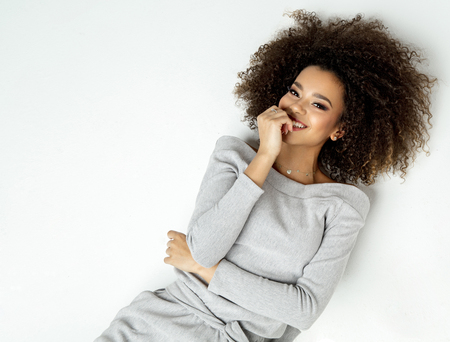 Portrait Of Beautiful Smiling Black Woman With Fresh Face, Soft Skin Having Fun Lying On White Backgroundの写真素材