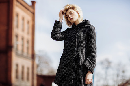 Fashion woman photo of young pretty girl touching her hair and posing outdoor in coat, spring street fashionの写真素材