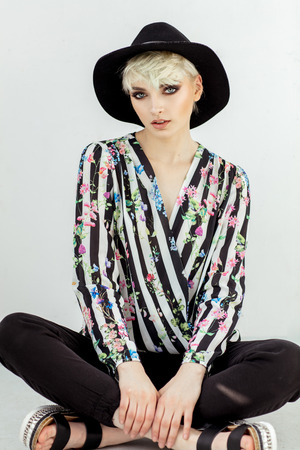 Beauty portrait of fashion blond model in a hat sitting on the floorの写真素材