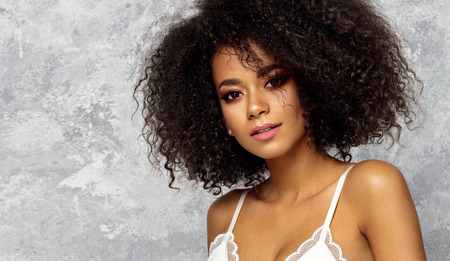 Beautiful black woman with an afro hairstyle wear white bra and looking at cameraの写真素材