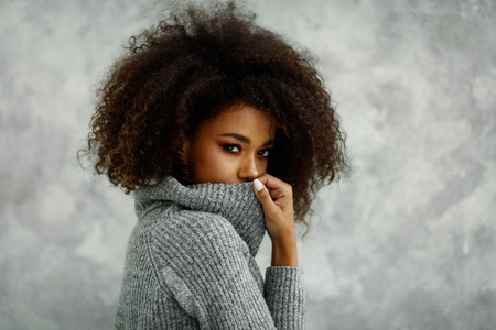 Portrait of young african american woman with an afro hair wear high-neck wool and cashmere sweater, hiding her mouth under the golfの写真素材
