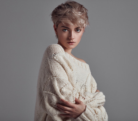 Portrait of young girl with blond hair wear sweater looking at camera isolated on gray backgroundの写真素材