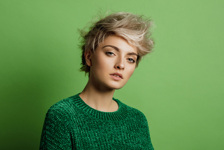 Fashion portrait of young woman with blond short hair isoalted on green backgroundの写真素材