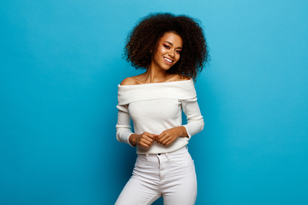 Beautiful black woman with white teeth and afro is smiling isolated on blue backgroundの写真素材