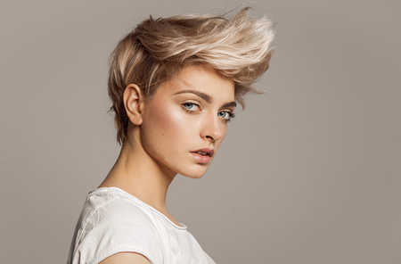 Portrait of young girl with blond fashion hairstyle looking at camera isolated on gray backgroundの写真素材