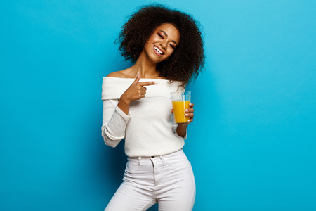 Beautiful smiling african american girl showing a glass of orange juiceの写真素材