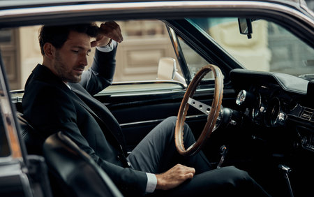 Handsome man in black suit sitting in the classic car