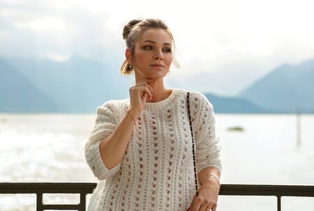 Beautiful young woman outdoor on a background of lake and mountains holding her hand near her faceの写真素材