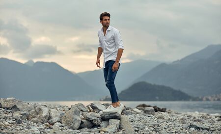 Fashionable male model walking on the stony beach over alps mountain viewの写真素材