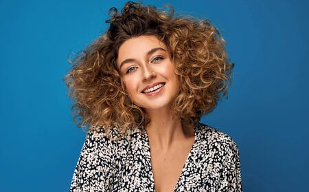 Portrait of young woman with blonde curly hair isolated on blue backgroundの写真素材