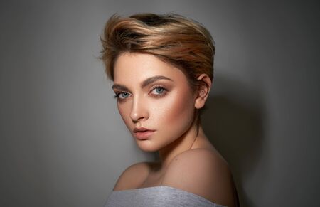 Portrait of young girl with blond fashionable hairstyle looking at camera isolated on gray backgroundの写真素材