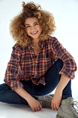Young smiling woman with blonde curly hair wear cotton check shirt and sitting on white backgroundの写真素材