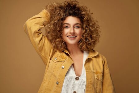 Happy young woman with curls posing at studio on brown studio background. Blonde woman with afro hairstyle smilingの写真素材