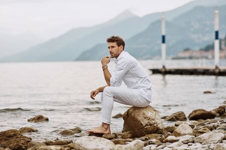 Handsome male model sits on a background of lake and mountainsの写真素材