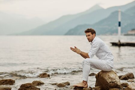 Handsome male model sits on a background of lake and mountainsの写真素材