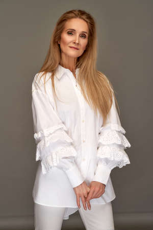 Mature female model with long straight hair wearing white stylish shirt over gray studio backgroundの写真素材