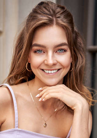 Portrait of beautiful smiling girl touching chin and looking at cameraの写真素材