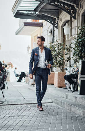 Handsome man in checked suit walking on the street with newspaperの写真素材