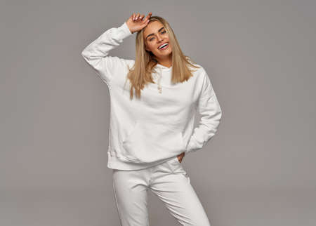 Beautiful young blonde woman wear of white set of track suit over gray backgroundの写真素材